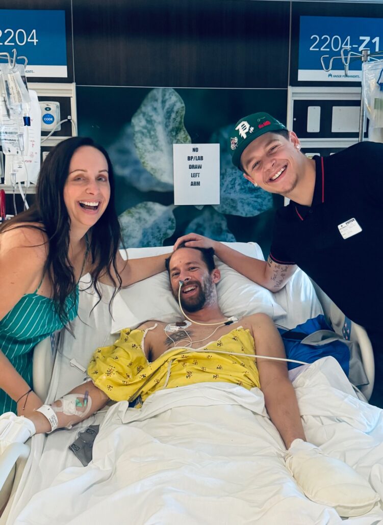 Jason Ellefson lies in a hospital bed smiling with his wife Shawna and her son.