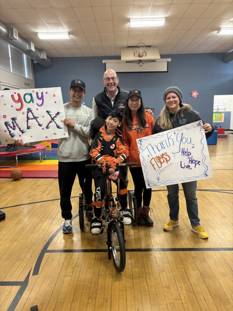 13-year-old Max Peng and his family receive an orange adaptive bike with Brad Marsh and Sonny Mullen.