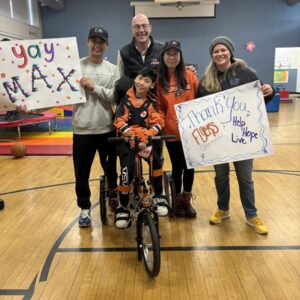 13-year-old Max Peng and his family receive an orange adaptive bike with Brad Marsh and Sonny Mullen.