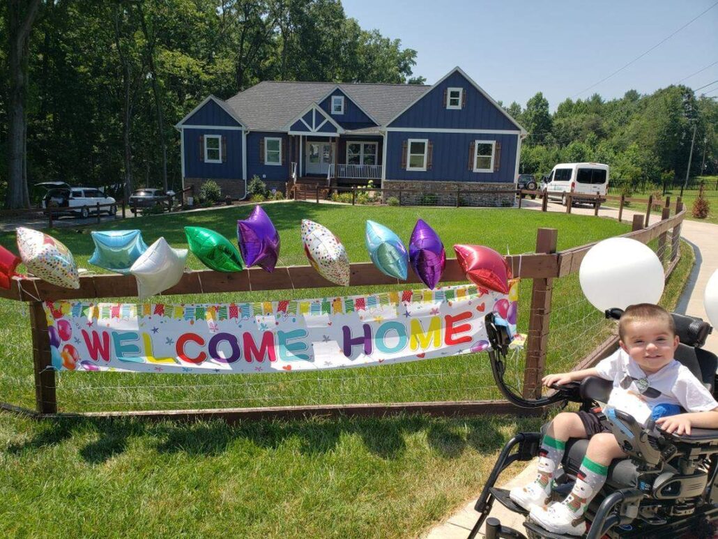 Logan Reese returns home with a Welcome Home sign and balloons. He is seated in his power chair.