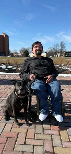 Scott Anthony Hughes seated in his wheelchair with his dog outside.