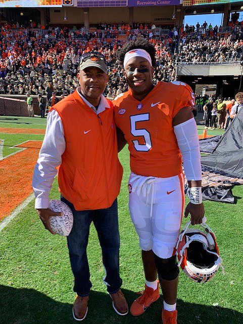 Keith Henry with son KJ Henry dressed in Clemson orange football uniform on the football field.