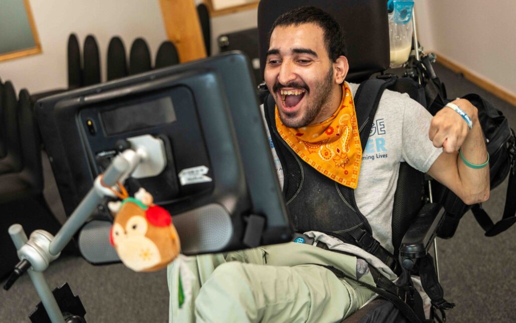 Yonan Matti grins as he uses his eye-gaze technology and sits in his power chair during an interview with the Times of San Diego in April 2026.
