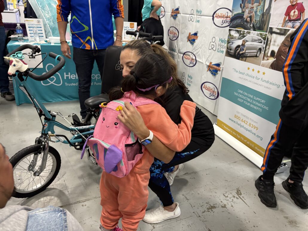 A hug from Kelly L Green with bike recipient Jeanney at Abilities Expo NY 2026.