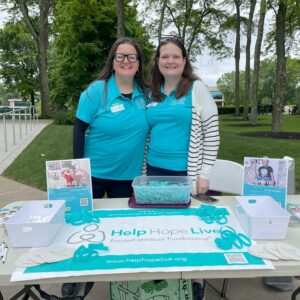 In matching polo shirts, Liz Casperite and Linda Jara staff a Help Hope Live table with signs, bracelets, and more.