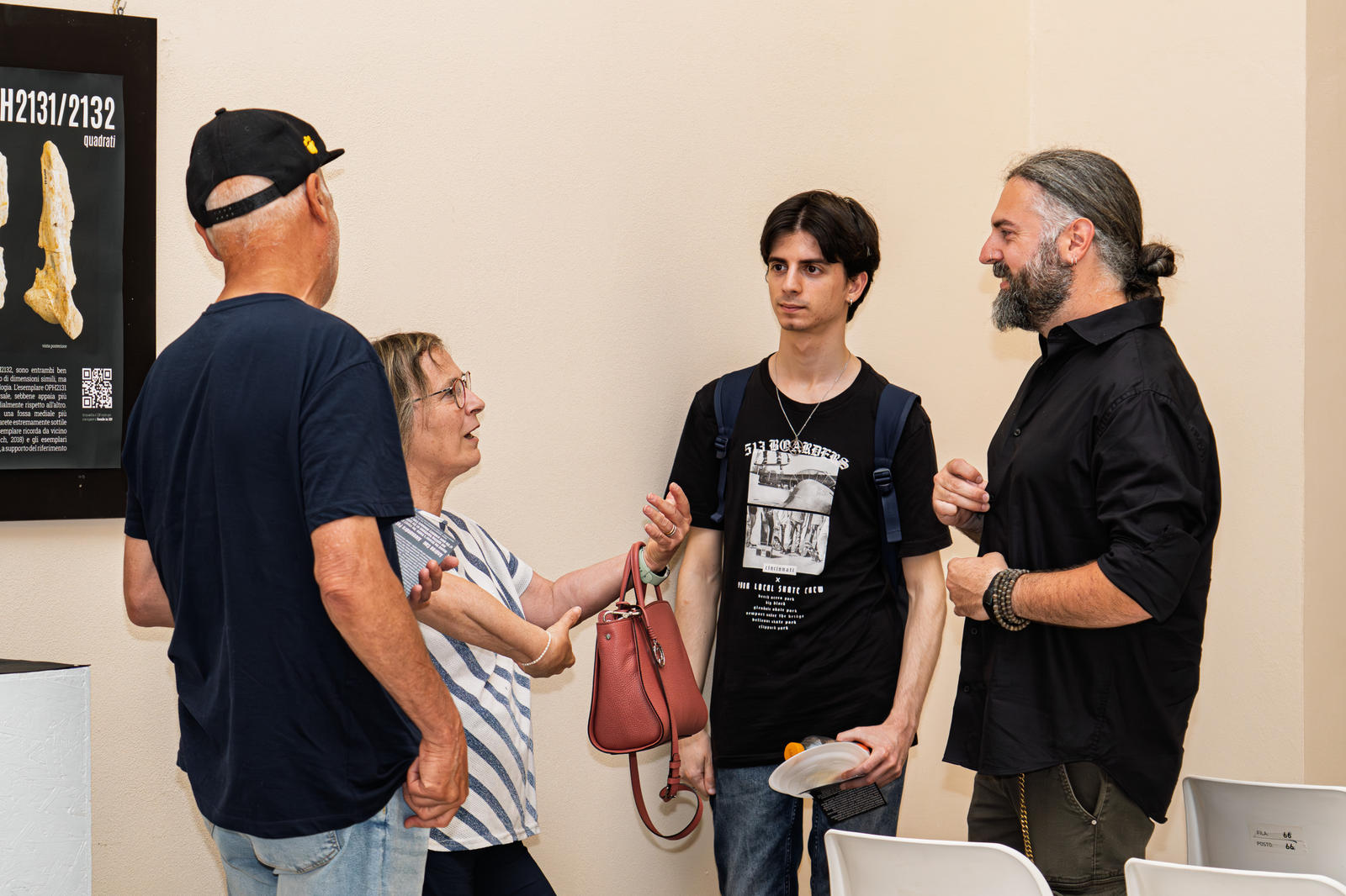 Partecipanti alla conferenza che parlano accanto a un pannello stampato con il reperto