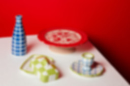 A close-up shot of the exclusive Vaisselle collection, with an egg cup, butter dish, cake stand, and oil pourer against a red and white backdrop