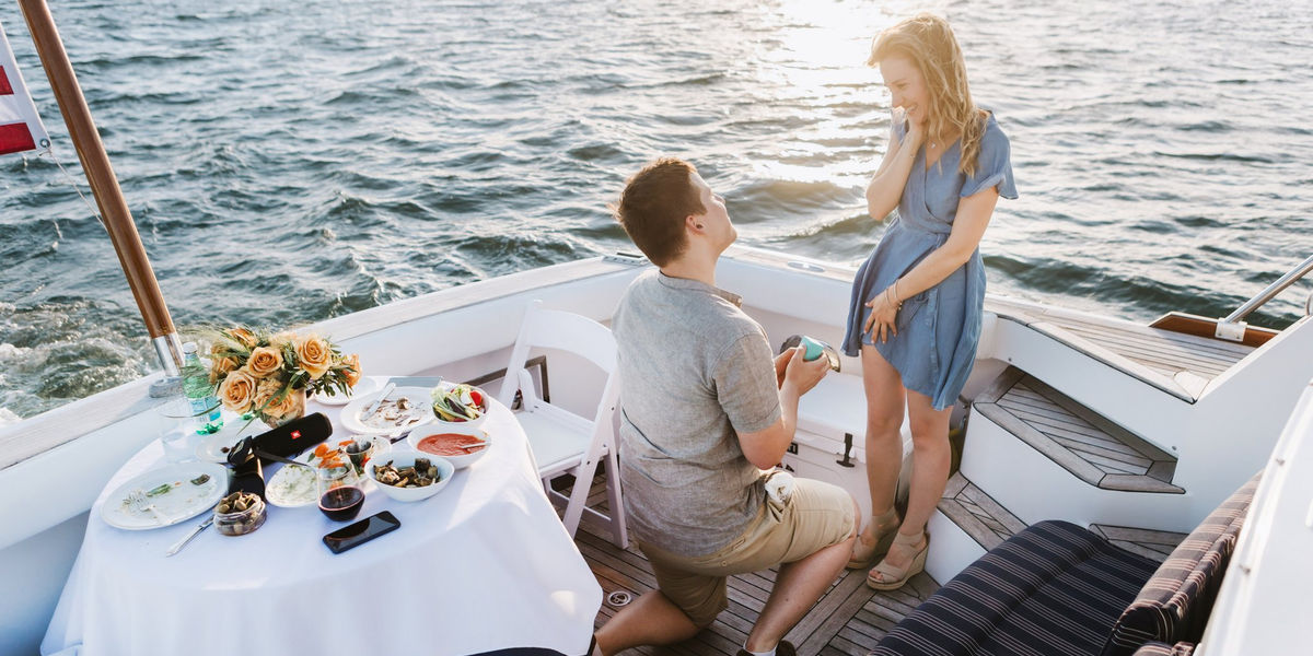 Gün batımında teknede evlilik teklifinden sonra sarılan çift.
