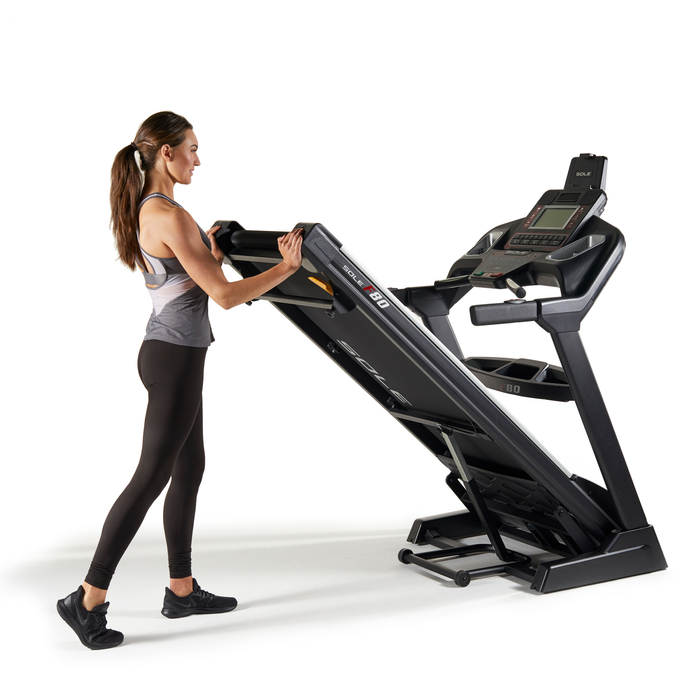 A young woman folding the Sole F80 treadmill
