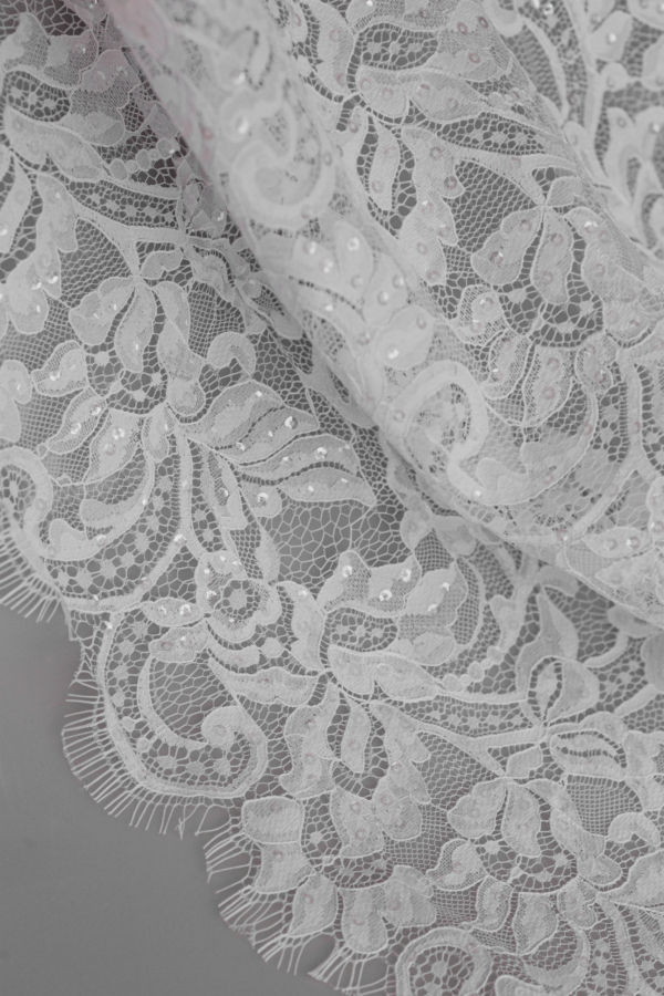 Biała koronka z motywem kwiatowym i drobnymi cekinami, widok zbliżenia materiału