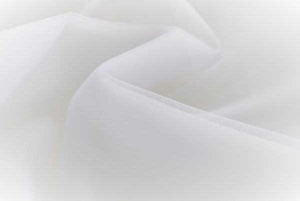 Zbliżenie białego, lejącego tiulu z delikatnym połyskiem, ukazujące jego miękką fakturę