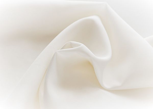 Gładka, kremowa satyna w odcieniu ivory, delikatnie pofałdowana, ukazująca połysk materiału