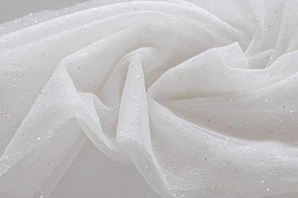 Biały tiul z drobnymi srebrnymi drobinkami brokatu, układający się w miękkie fale