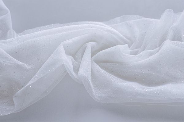 Biały lejący tiul z drobnym brokatem, delikatnie pofałdowany na jasnym tle