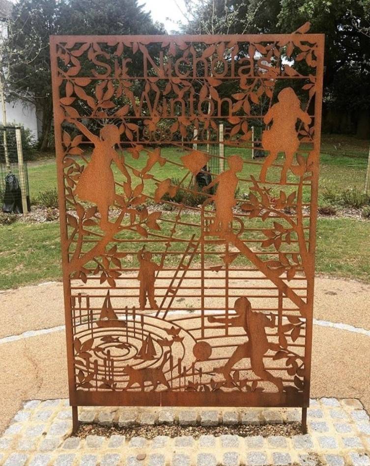 Metal memorial showing Nicholas Wintons name, with children playing games