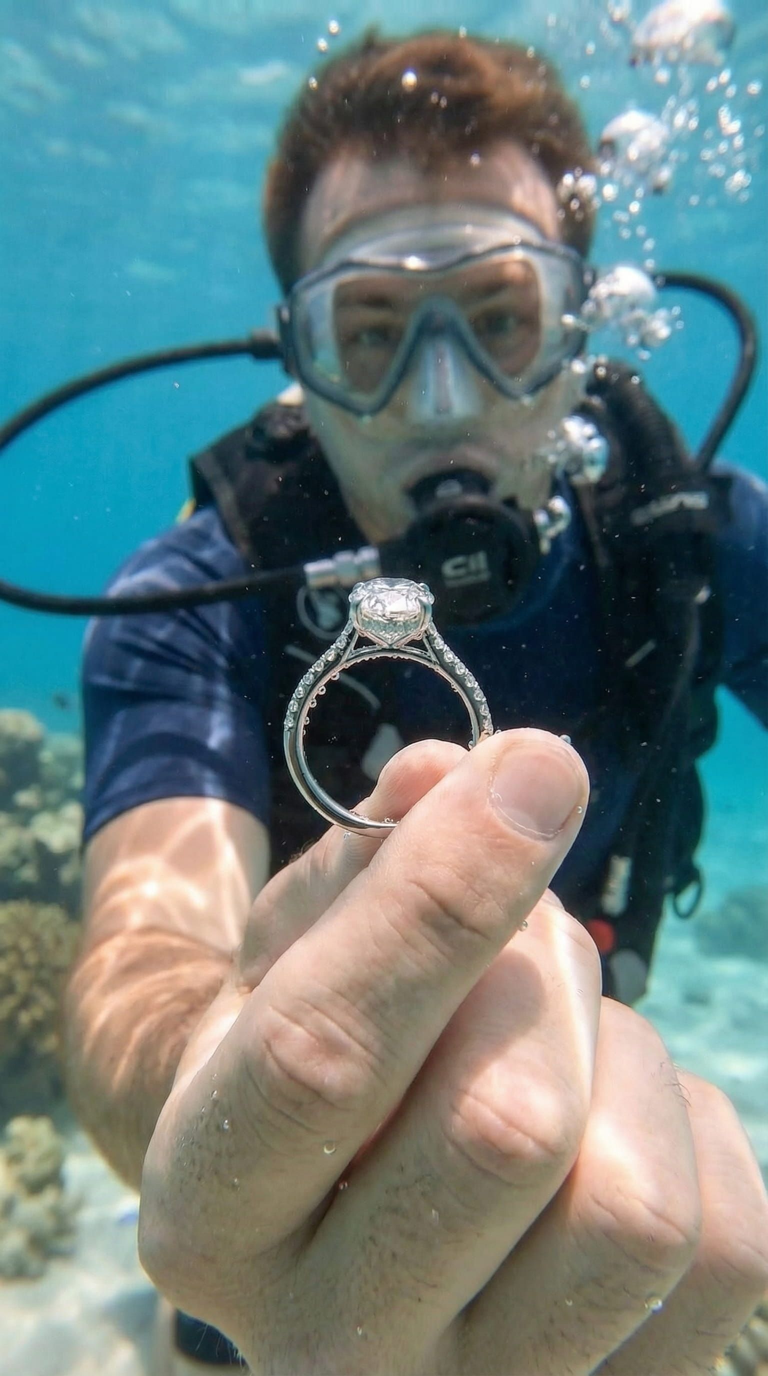 Photorealistic AI generated image of a scuba diver presenting a diamond engagement ring underwater, highlighting the sparkling diamond and the romantic setting, AI jewelry photography style.