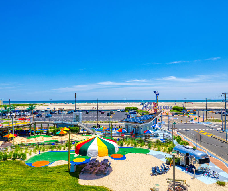 Aerial view of a colorful mini golf course near a beach with a parking lot and ocean in the background.