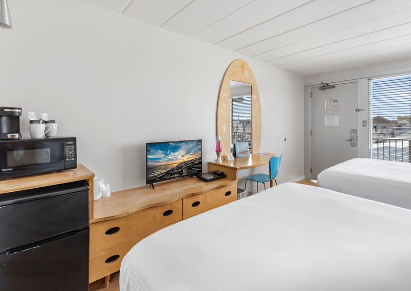 A hotel room with two beds, a wooden desk, a small fridge, and a microwave.
