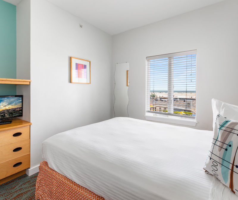 A hotel room with a bed, window, dresser, and TV.