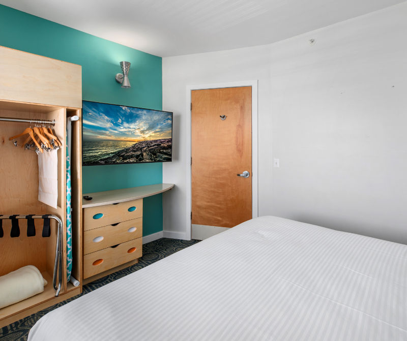 A hotel room with a bed, TV, closet, and dresser