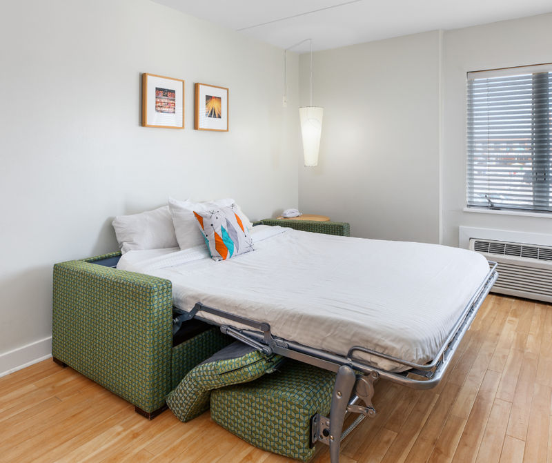 A guest room with a sofa bed, wood flooring, and white walls