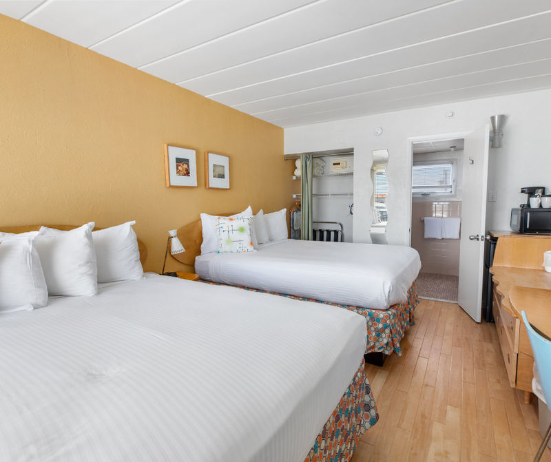 A hotel room with two queen beds, a desk, and a bathroom doorway.