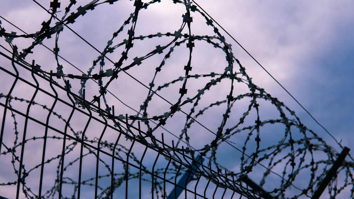 The fence of the correctional facility with barbed wire on the background of a gloomy cloudy dark blue sky.