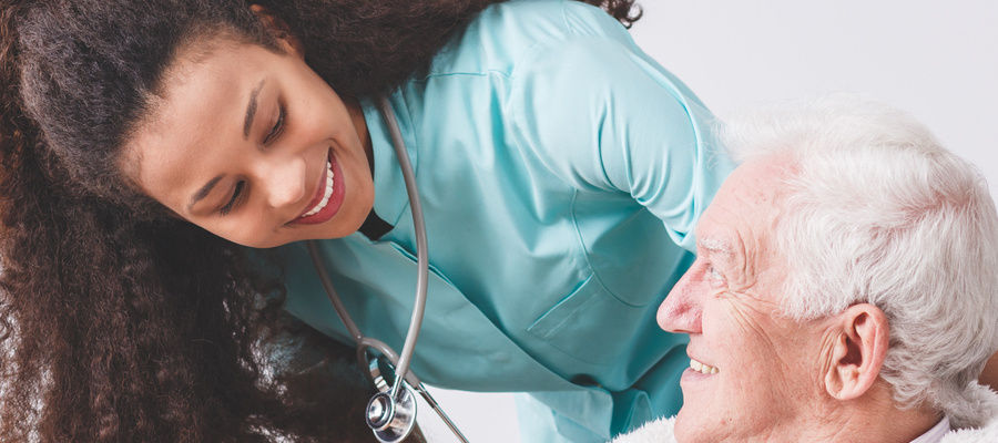 Panorama of a happy nurse with a stethoscope covering an elderly man with a blanket in a nursing home