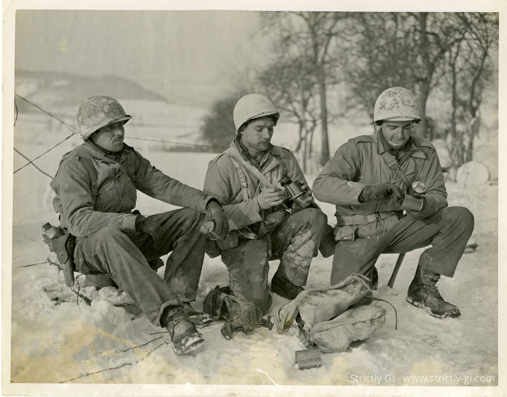 Mortar squad of the Company E, 2d Battalion, 8th Infantry Regiment (4th Infantry Division) pause to eat C Rations near Bettendorf, Luxembourg. 
L-R: Private First Class Ray Cottingham (Kokomo, Indiana); Private John W. West (Atlanta Georgia); and Private James J. Kudrne, Jr. (Brookfield, Illinois).