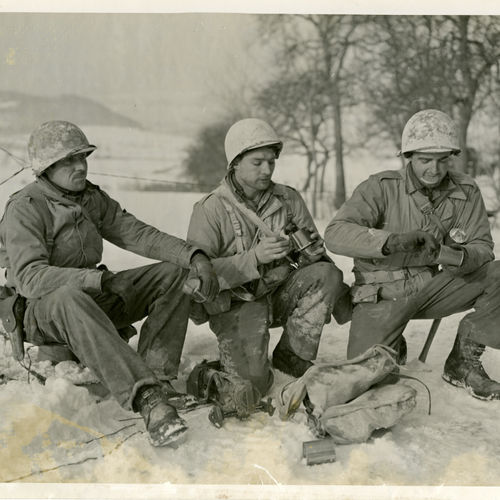 Mortar squad of the Company E, 2d Battalion, 8th Infantry Regiment (4th Infantry Division) pause to eat C Rations near Bettendorf, Luxembourg. 
L-R: Private First Class Ray Cottingham (Kokomo, Indiana); Private John W. West (Atlanta Georgia); and Private James J. Kudrne, Jr. (Brookfield, Illinois).