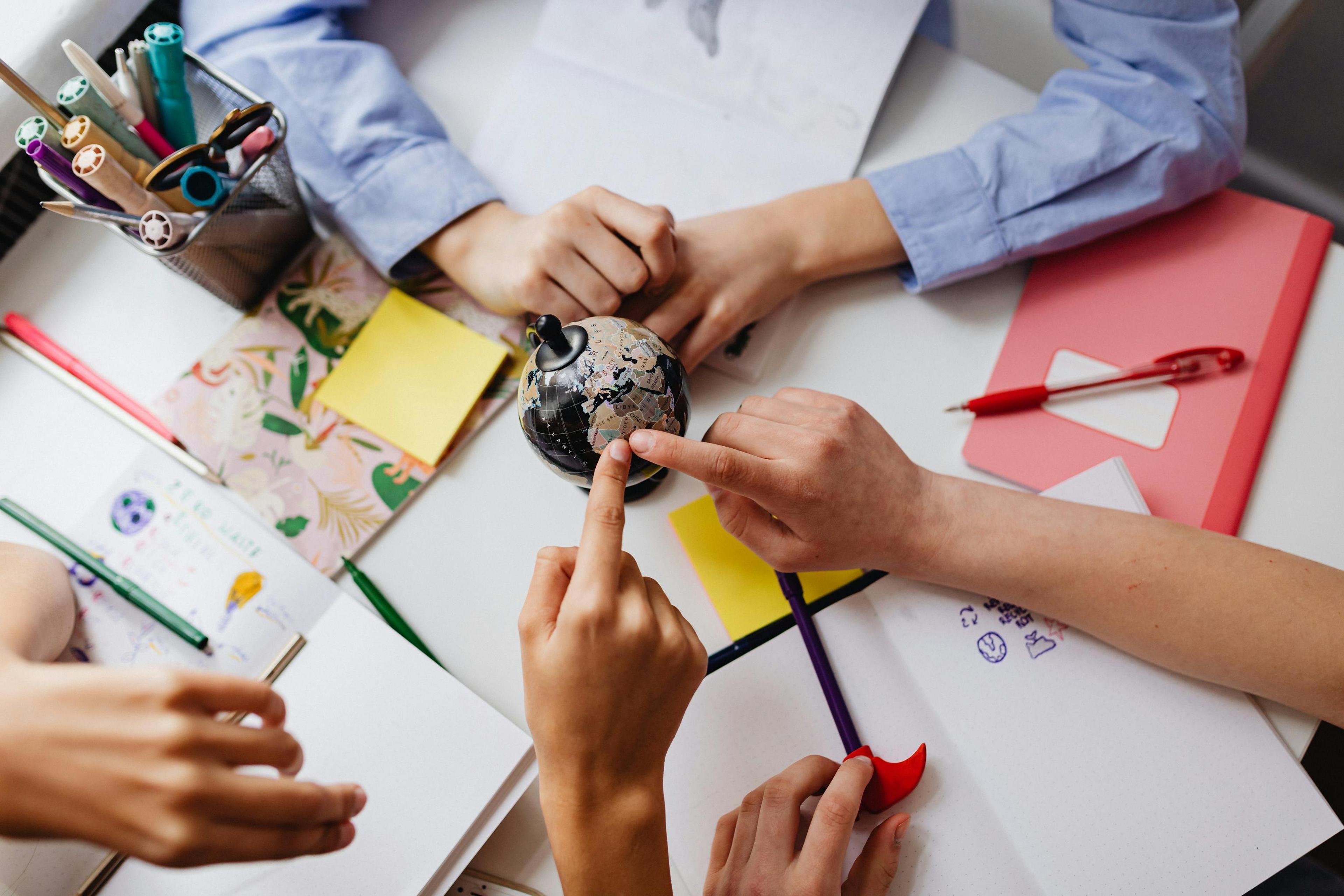 Students collaborating hands-on — sketches, notes, and a small globe on a shared desk