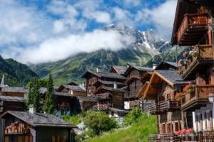 brown wooden houses near green trees and mountain under white clouds during daytime