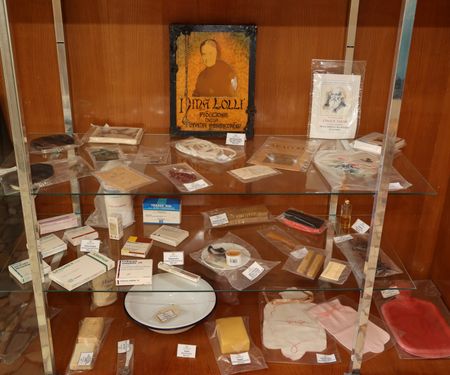 Foto 13 e 14: (metà pagina)	VETRINA DEI RICORDI in cui si custodiscono oggetti appartenuti alla Serva di Dio (corona del Rosario, cingolo, regola, immaginette, farmaci, catino, forcine, ventaglio, profumo, sapone, scialle, calze e fazzoletti, abito e pantofole, filo e aghi per il ricamo, squadre, matite e bozze dei disegni da ricamare,…
