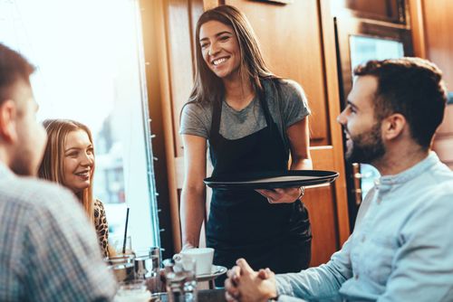 Cameriera sorridente serve i clienti al tavolo.