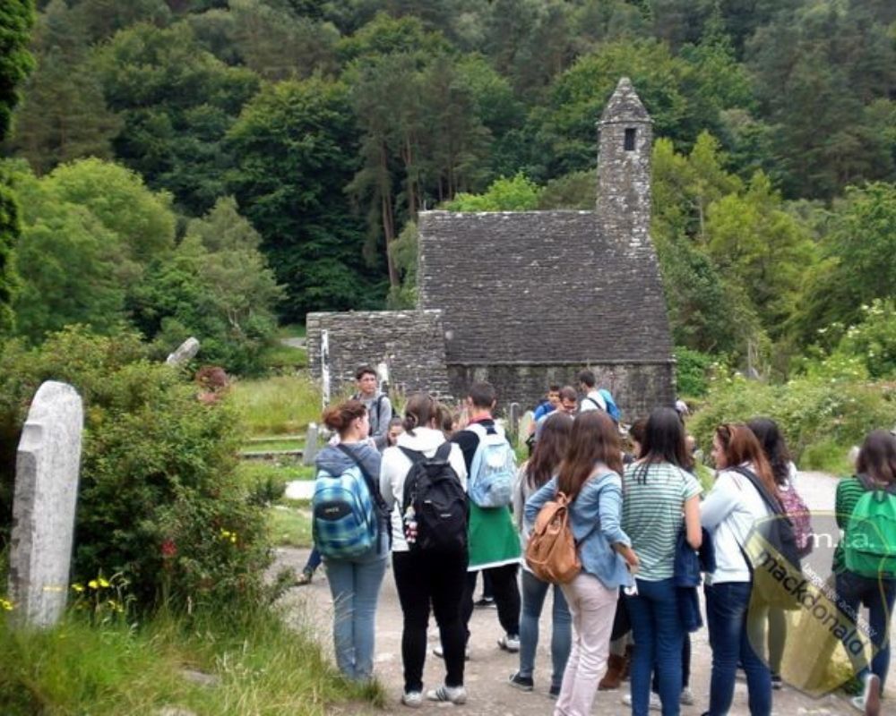 Ragazzi partecipano a un escursione con una cappella in pietra sullo sfondo.
