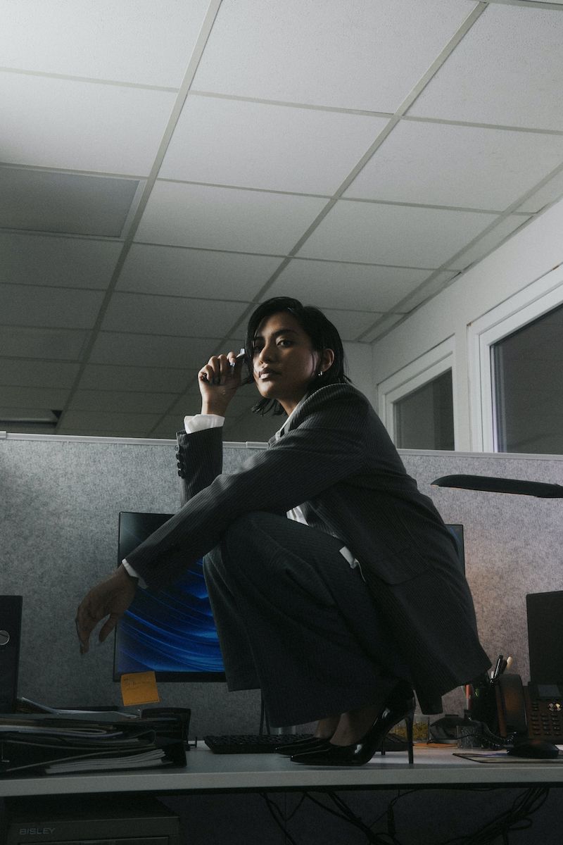 photo of a very cool human in a suit crouched on a desk in an office (but professional)