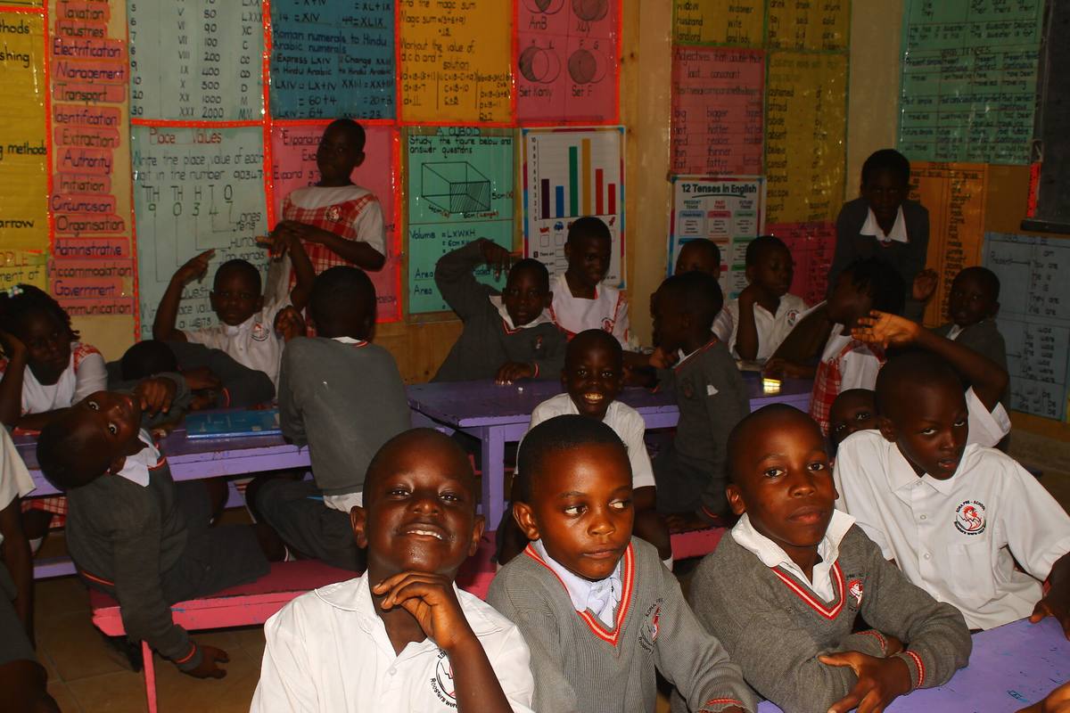 Pupils at painted desks in a classroom lined with handmade teaching charts