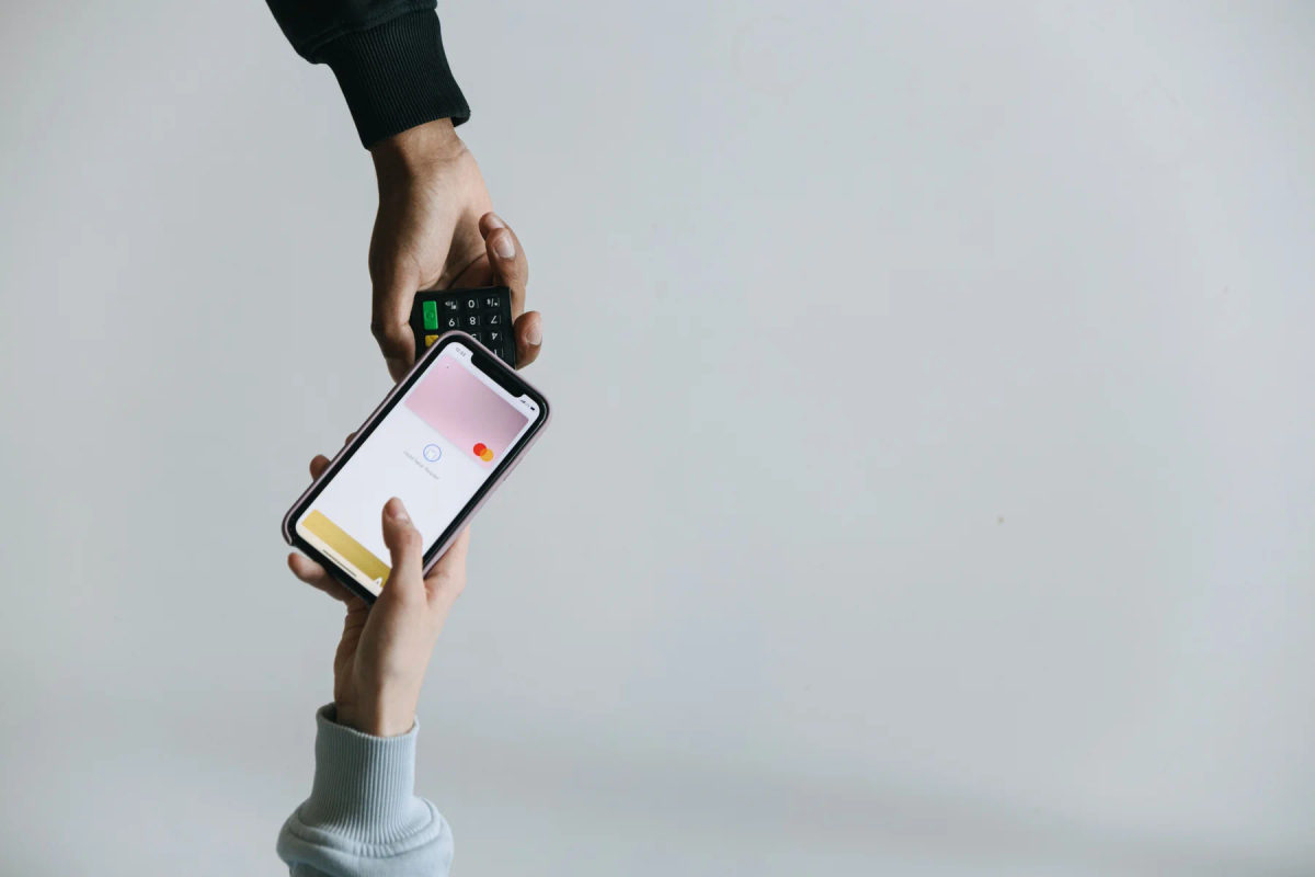 Hands hold a smartphone near a card payment terminal.