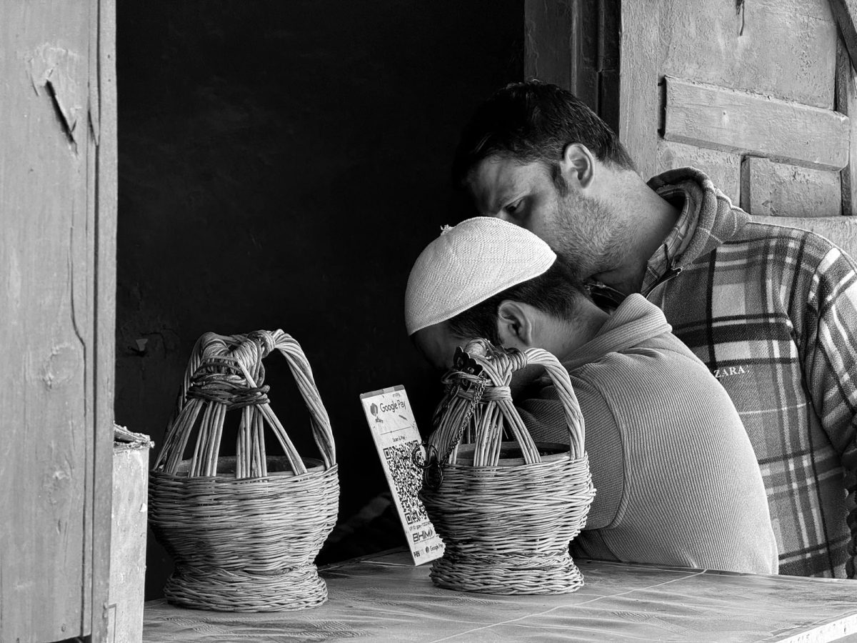Two men at a Kishtwar market stall look at a BHIM UPI QR payment sign.
