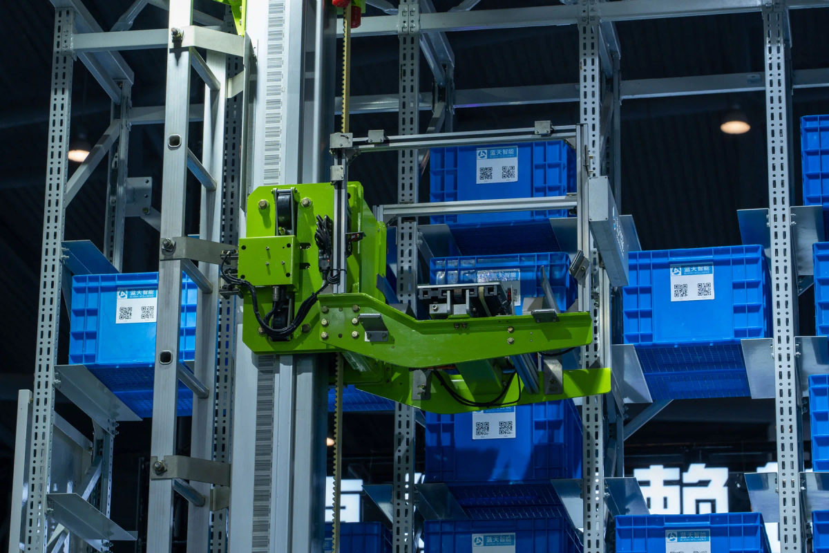 A green robotic arm handles storage crates in an automated warehouse.