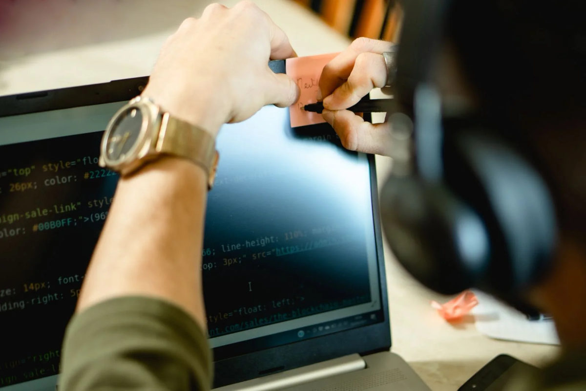 A person writing a note beside a computer screen while working.