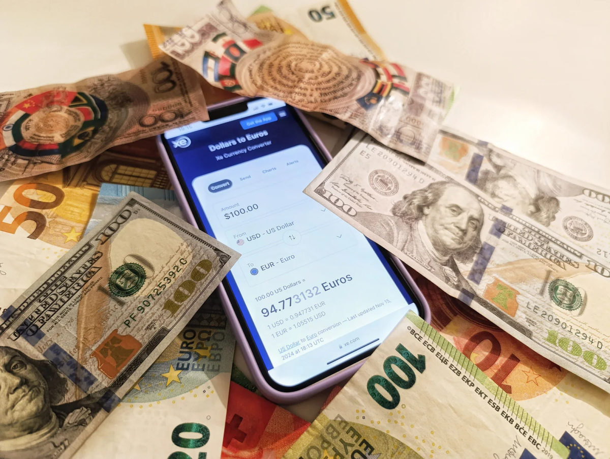 A phone currency-converter screen surrounded by U.S. dollar and euro banknotes.