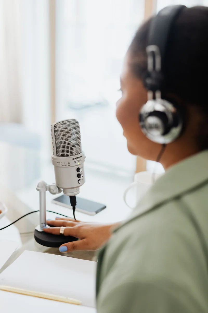 A woman recording a podcast with a microphone and headphones; illustrative live-audio context, not Gemini.