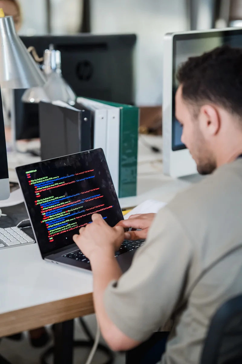 Software developer types code on a laptop in an office.
