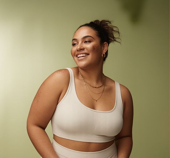 Smiling woman in a cream sports bra against a soft green backdrop