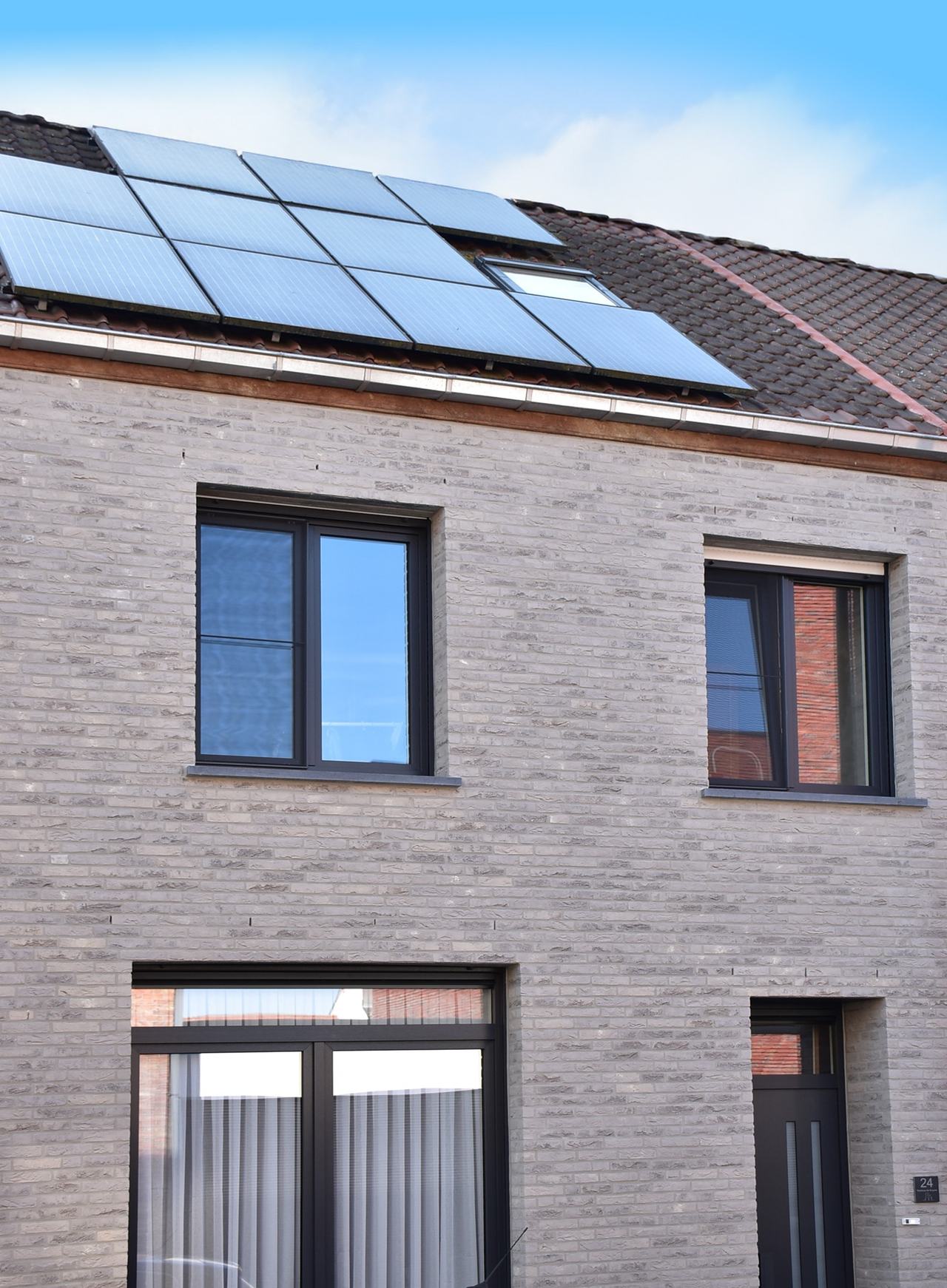 De nieuwe gevel over twee bouwlagen met zwart buitenschrijnwerk, onder het bestaande bruine pannendak waarop al zonnepanelen en een dakvlakvenster liggen