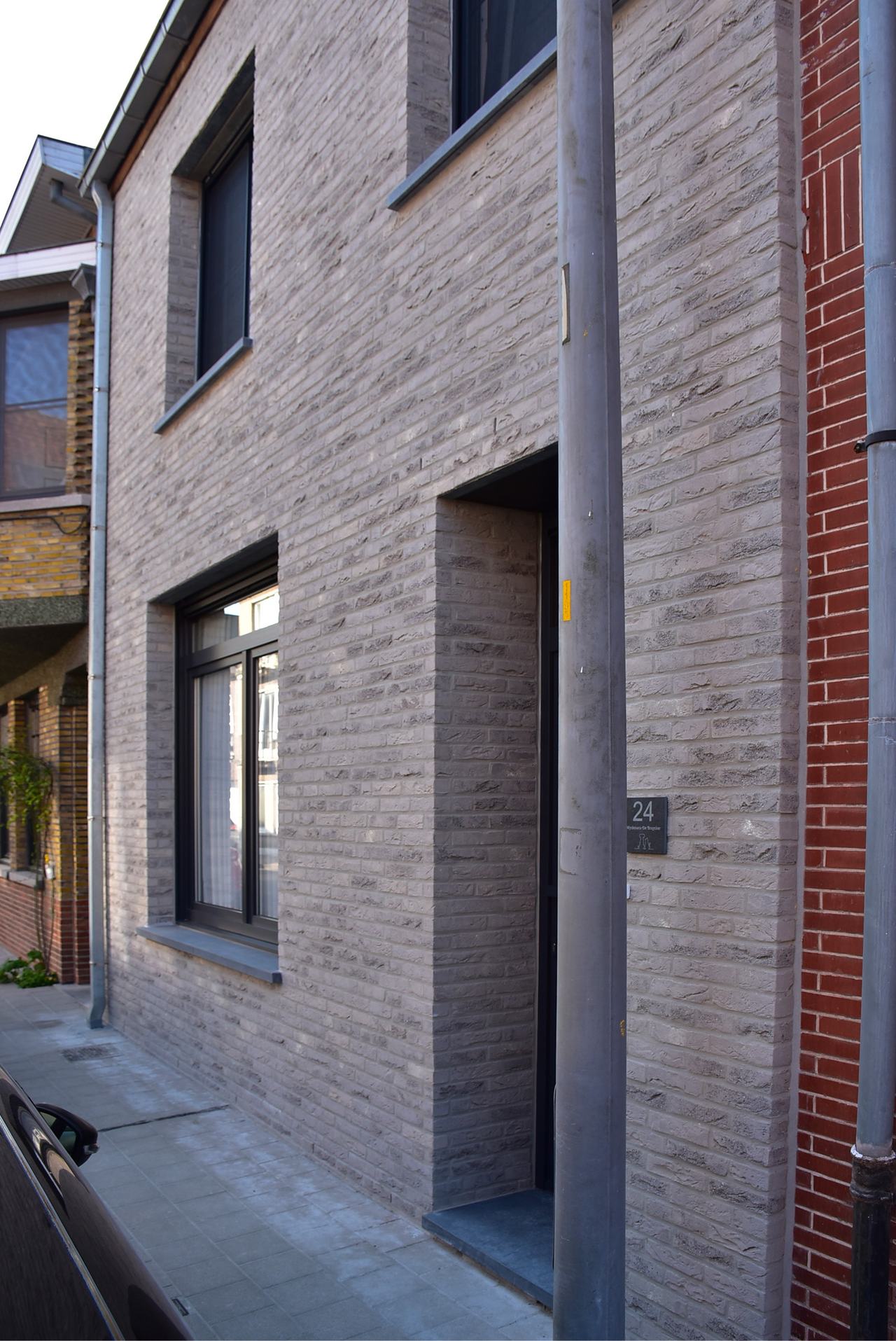 Voorgevel van een woning in Oostkamp in grijsbeige gevelsteen met zwart buitenschrijnwerk, een teruggetrokken inkom en donkergrijze stenen dorpels