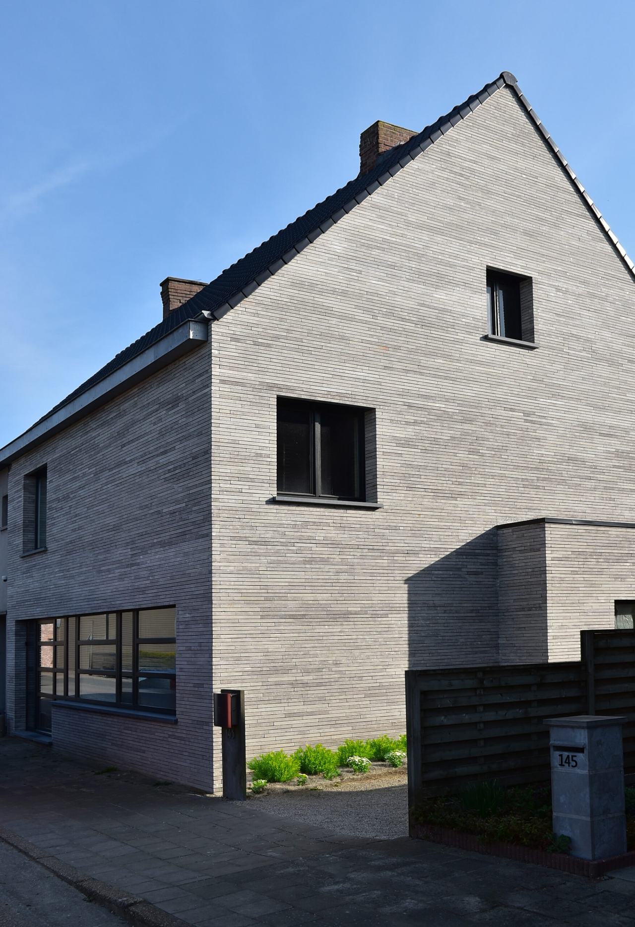 Woning in Veldegem met een puntgevel volledig gemetst in lichtgrijze tot beige langformaatsteen, met zwart buitenschrijnwerk onder een donker pannendak
