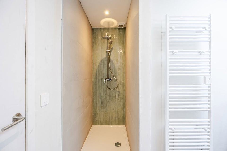 Smalle douche met een achterwand in groene zellige tegels, zijwanden in grootformaat beige tegels en een vlakke witte douchebak