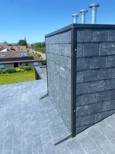 Schouw volledig bekleed in natuurleien met drie metalen schouwbuizen erboven, afgewerkt met een donker hoekprofiel op de hoek, staand op een dak in dezelfde leien